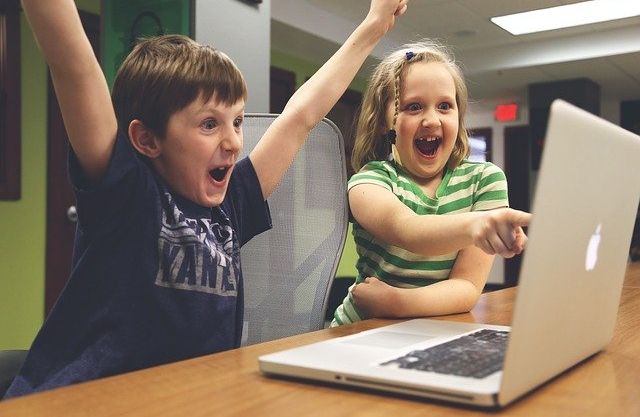 Excited children cheering while looking at a computer monitor